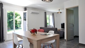 A modern living room with a wooden dining table, white chairs, a grey sofa, and a TV.