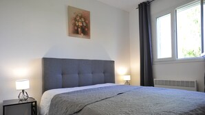 A bedroom with a large bed, two bedside lamps, a painting on the wall, and a window with curtains.