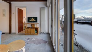 A room with a large window, a wooden TV stand, a star-patterned rug, and a door leading to another room. - Appartement Savoleyres 10 - La Tzoumaz, 4 Vallees (La Tzoumaz)
