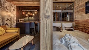 Quarto de hotel moderno com teto de madeira, sofá, cama, escrivaninha e uma janela grande.