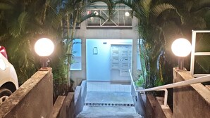 Una escalera conduce a un edificio de techo inclinado, rodeado de palmeras.