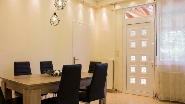 A dining area with a wooden table and black chairs, a white door with glass panels, and hanging light fixtures. - Feel the nature! (Rethymno)