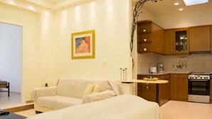 A hotel room with a sofa, a bed, a small table, and a kitchenette with a stove and cabinets. - Feel the nature! (Rethymno)