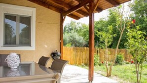 A covered patio with a glass table and chairs, a window, and a wooden fence in the background. - Feel the nature! (Rethymno)