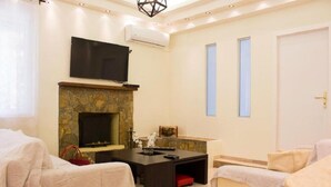 A modern hotel room with a stone fireplace, a flat-screen TV, a dining table, and two beds. - Feel the nature! (Rethymno)