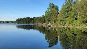 Un lac paisible, avec une jetée qui s’avance sur l’eau, entouré d’une forêt dense et bordé d’un ciel dégagé.
