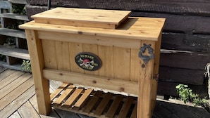 Un banc en bois surmonté d’un panneau représentant un crâne et des tibias croisés, placé sur une terrasse en bois.