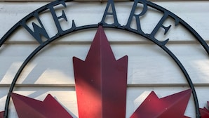 Un panneau circulaire avec une feuille d’érable rouge et le texte « NOUS SOMMES CANADIENS » sur un fond blanc.