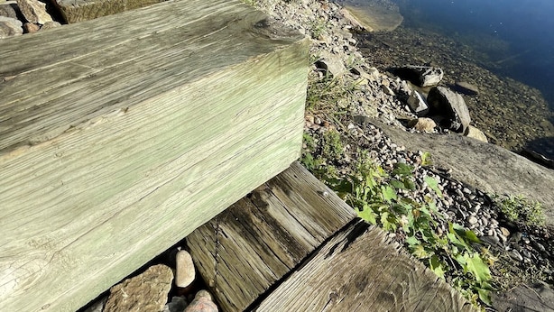 Une terrasse en bois bordée de pierres, qui mène à un lac paisible entouré d’arbres.