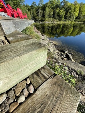 Une terrasse en bois bordée de pierres, qui mène à un lac paisible entouré d’arbres.
