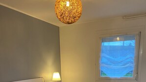 A bedroom with a large bed, a bedside lamp, a window with a view, and a textured ceiling light. - Le Mathiez (Dijon)