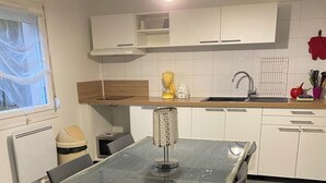 A modern kitchen with white cabinets, a glass dining table, and a coffee maker on the counter. - Le Mathiez (Dijon)