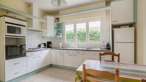 Une cuisine avec des meubles blancs, un four à micro-ondes, une cuisinière et une fenêtre donnant sur un paysage verdoyant.