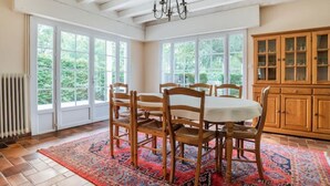 Un coin repas comprenant une table et des chaises, de grandes fenêtres et un buffet en bois.