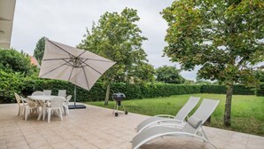 Une terrasse extérieure avec une table et des chaises, un barbecue et des fauteuils de jardin.