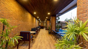 A covered outdoor seating area with brick walls, wooden flooring, and potted plants. - Blanc Smith Hotel  (Siem Reap)