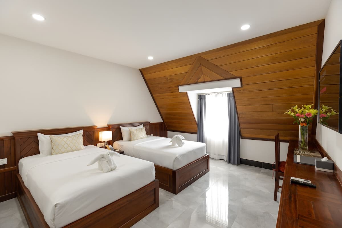 Habitación de hotel con dos camas, techo de madera, escritorio con un florero y un espejo grande.