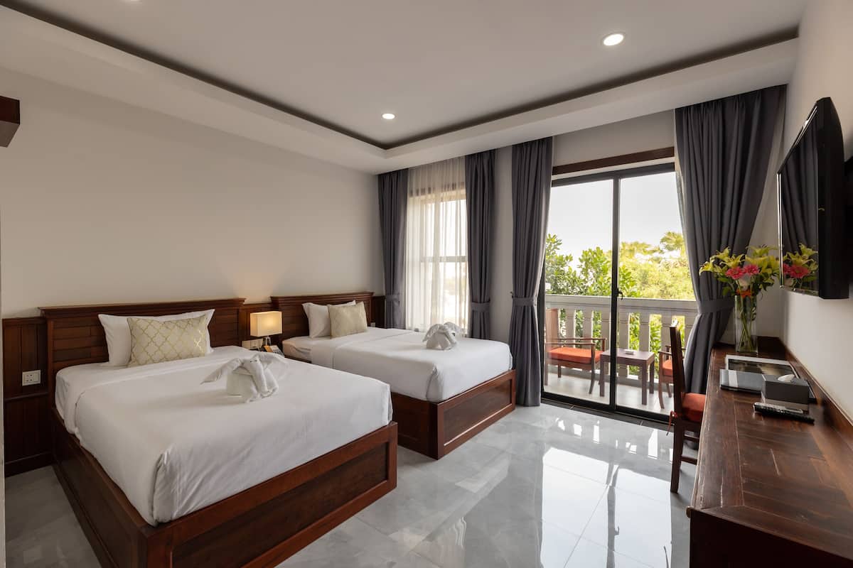 Una habitación de hotel con dos camas, un balcón, un escritorio con silla y una televisión.