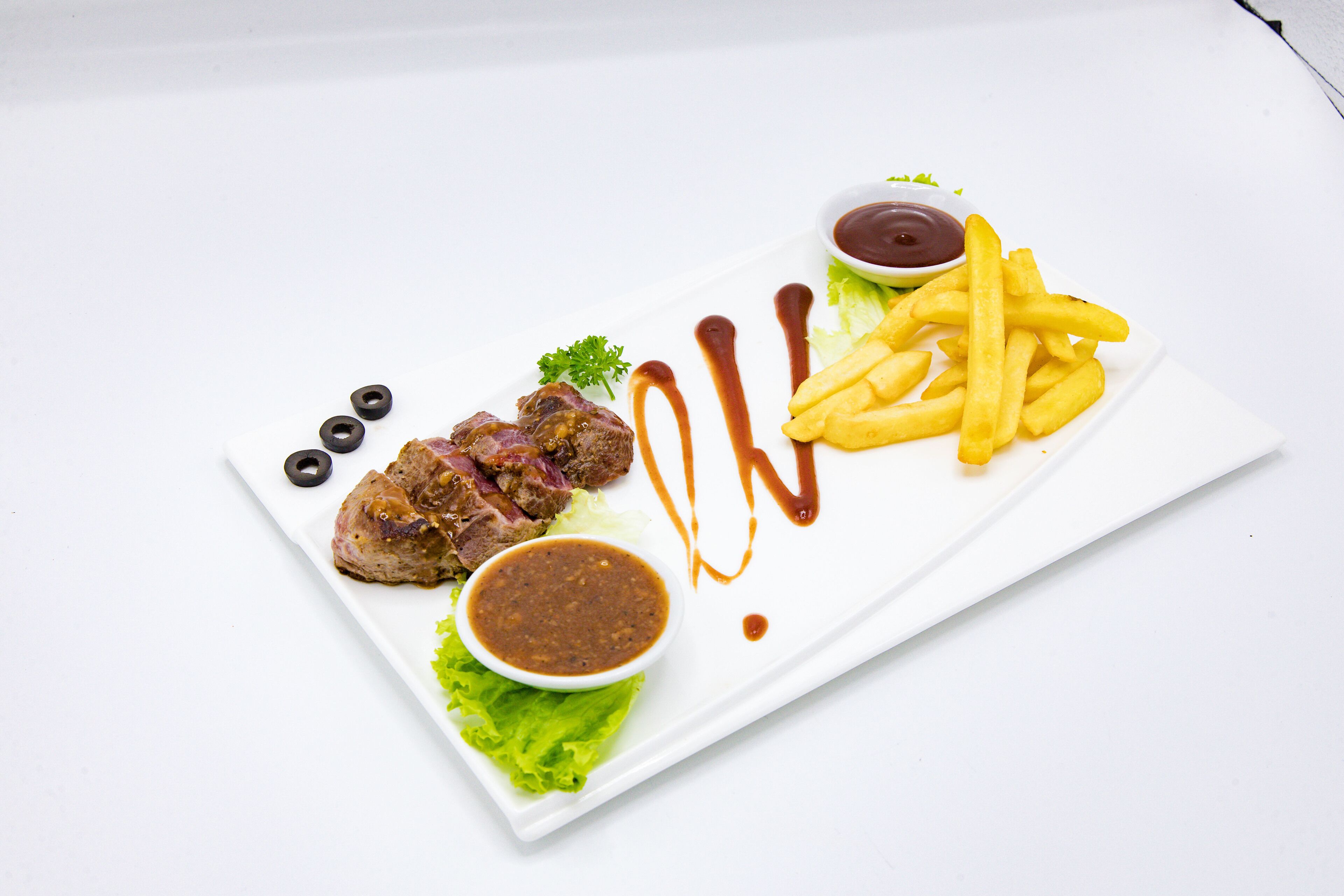 A white plate with steak, fries, and two dipping sauces.