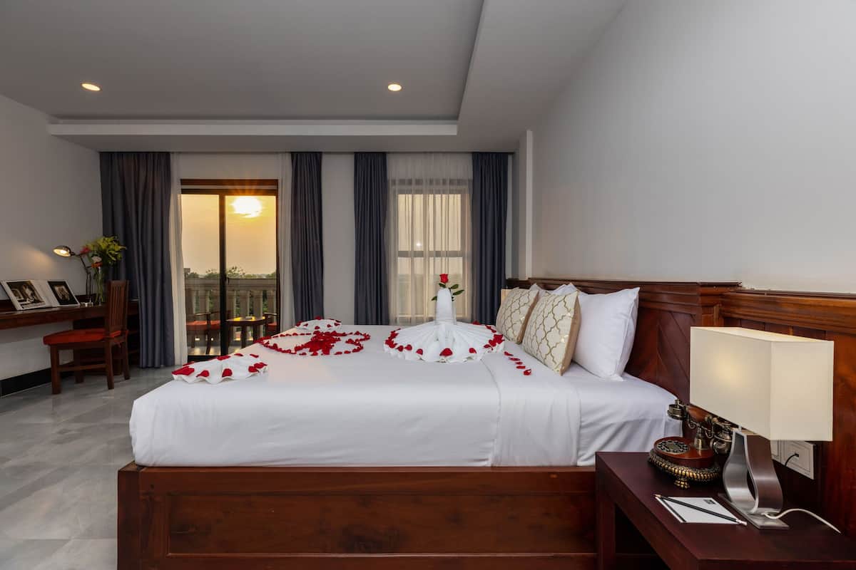 Una habitación de hotel con una cama grande, un escritorio con lámpara y vistas al atardecer a través de la ventana.