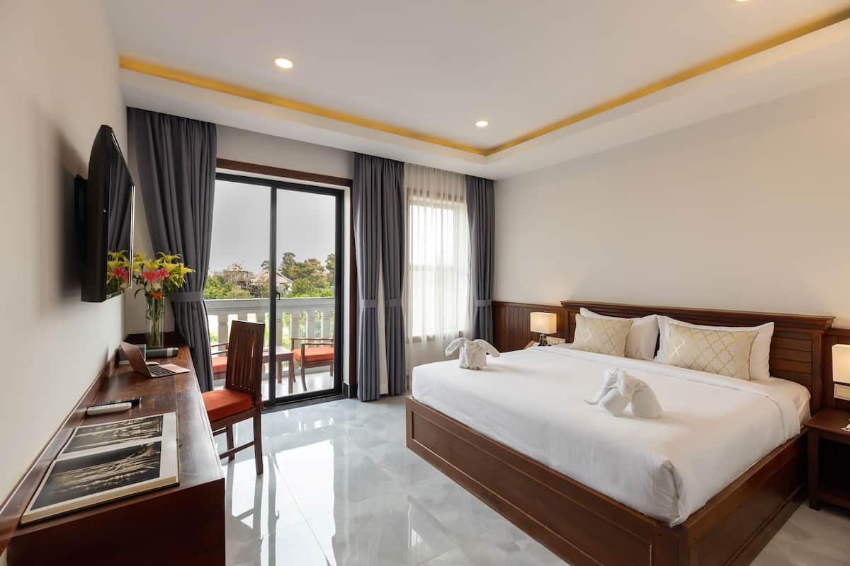 Habitación de hotel con una cama grande, un escritorio con una computadora portátil, una silla, un televisor y un balcón con cortinas.
