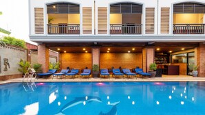 A swimming pool with blue tiles, surrounded by lounge chairs and a building with a balcony. - Blanc Smith Hotel  (Siem Reap)
