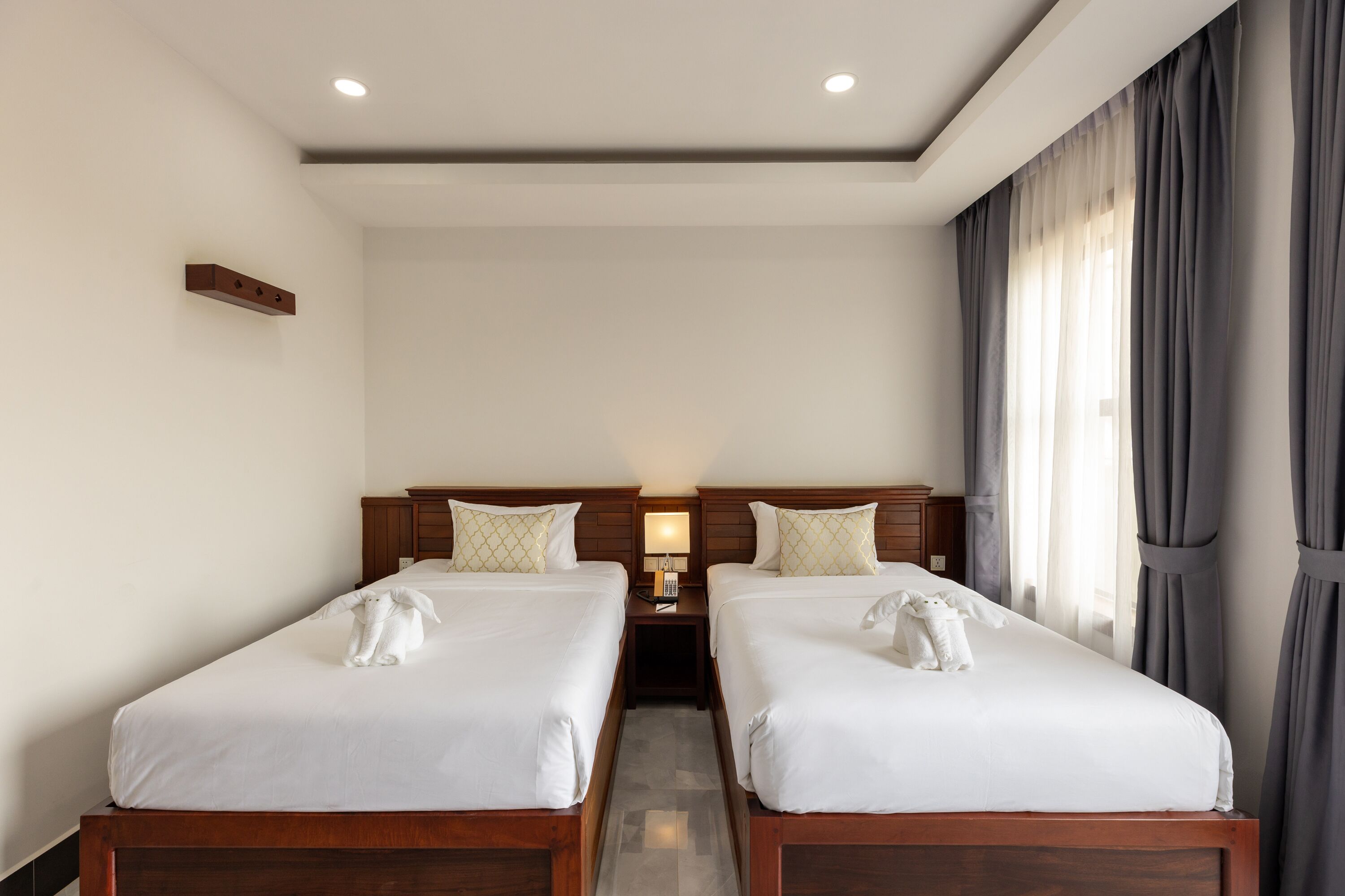 A hotel room with two single beds, a nightstand with a lamp, and a window with curtains.