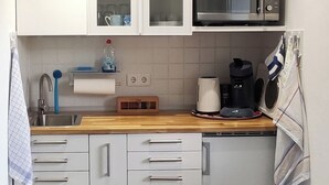 A compact kitchen with white cabinets, a microwave, a coffee maker, and a tea kettle. There are two drawers and a small trash bin. - Small, lovingly furnished vacation apartment with terrace (Taunusstein)