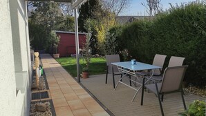 A patio with a table and chairs, a red shed, and a garden with various plants. - Small, lovingly furnished vacation apartment with terrace (Taunusstein)