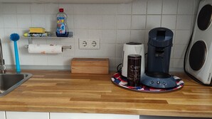 A kitchen with a stainless steel sink, a blue cleaning brush, a coffee maker, and a water heater. - Small, lovingly furnished vacation apartment with terrace (Taunusstein)