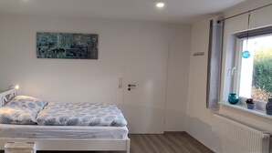 A bedroom with a bed, a window with a view, and a painting on the wall. - Small, lovingly furnished vacation apartment with terrace (Taunusstein)