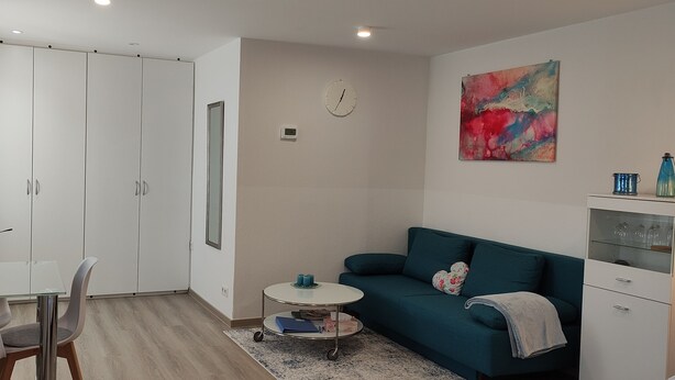 A modern living room with a teal sofa, a glass dining table, and a white wardrobe. - Small, lovingly furnished vacation apartment with terrace (Taunusstein)