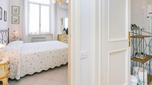 Une chambre à coucher comprenant un lit, une commode, une coiffeuse, un lustre et une fenêtre avec des rideaux.