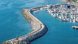 Un port de plaisance situé sur la côte, avec des bateaux amarrés, une digue rocheuse et une statue sur une petite île.
