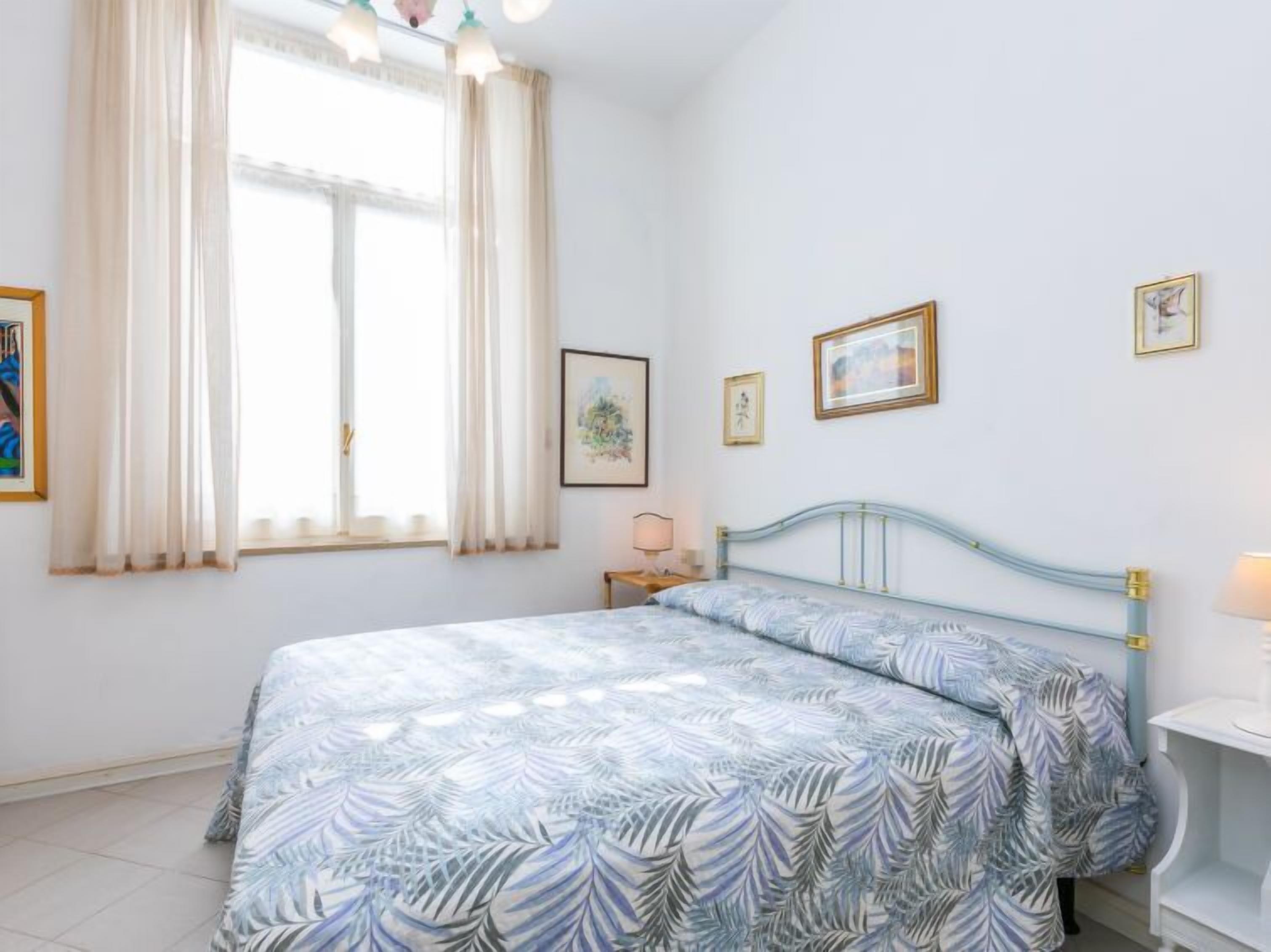 A bedroom with a bed, a window with curtains, and wall-mounted pictures.