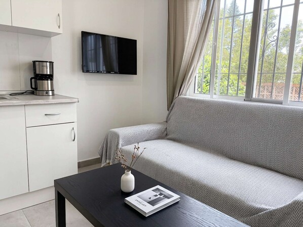 Ett modernt rum med en soffa, en kaffebryggare, en TV och ett fönster med gardiner.