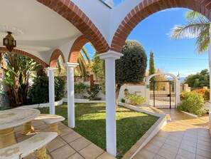 Une terrasse couverte avec des arches en briques, un sol carrelé et un petit jardin agrémenté d’une porte.