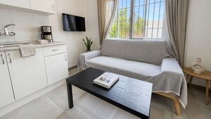 A modern living space with a sofa, a coffee maker, a flat-screen TV, and a window with curtains.