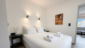 A modern hotel room with a large bed, two bedside tables, a nightstand, a vase with white flowers, and a painting on the wall.