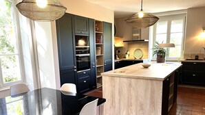 Een moderne keuken met donkerblauwe kastjes, een centraal eiland en een eethoek met een zwarte tafel en witte stoelen.