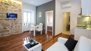 A modern living room with a stone accent wall, a dining area with white furniture, and a kitchen with a glass island. - Casa Arancia (Dubrovnik)