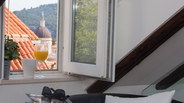 A room with a view of a building with a dome, a window sill with a glass of orange juice, and a magazine on a black couch. - Casa Arancia (Dubrovnik)