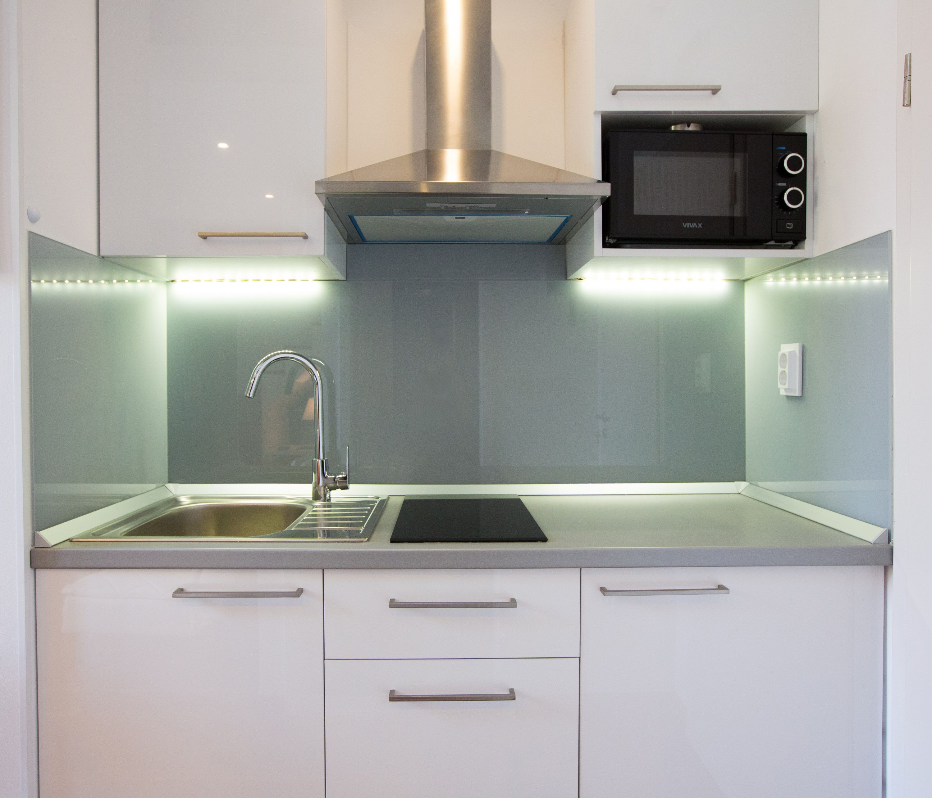 A modern kitchen with a stainless steel sink, a microwave, and a ventilation hood.