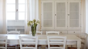 A dining area with a white table and chairs, a vase with flowers, and a white cabinet with louvered doors. - Cozy family apartment for 6 people. (Lazio)