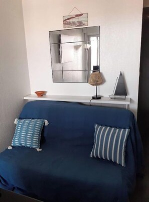 Um sofá azul com almofadas estampadas, uma mesinha com abajur e um objeto decorativo na parede.
