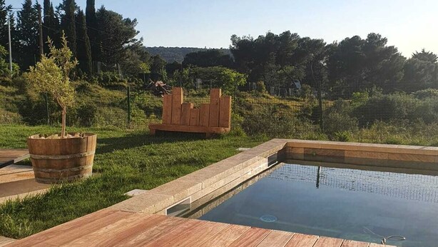 A wooden deck surrounding a rectangular pool with a stone border. - Villa Avec Piscine en Campagne Aixoise au Cœur du Village Provencal de Ventabren (Ventabren)