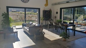 A spacious living area with a sofa, dining table, and chairs. There is a large window offering a view of the outdoors. - Villa Avec Piscine en Campagne Aixoise au Cœur du Village Provencal de Ventabren (Ventabren)