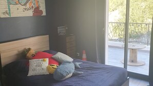 A bedroom with a bed, pillows, a stuffed toy, a wall art piece, a window, and a view of the outdoors. - Villa Avec Piscine en Campagne Aixoise au Cœur du Village Provencal de Ventabren (Ventabren)