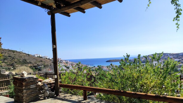 A stone-paved terrace with a wooden railing overlooking a coastal town and the sea.
