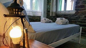 A room with a bed, a wooden table, a lamp, and a stone wall.
